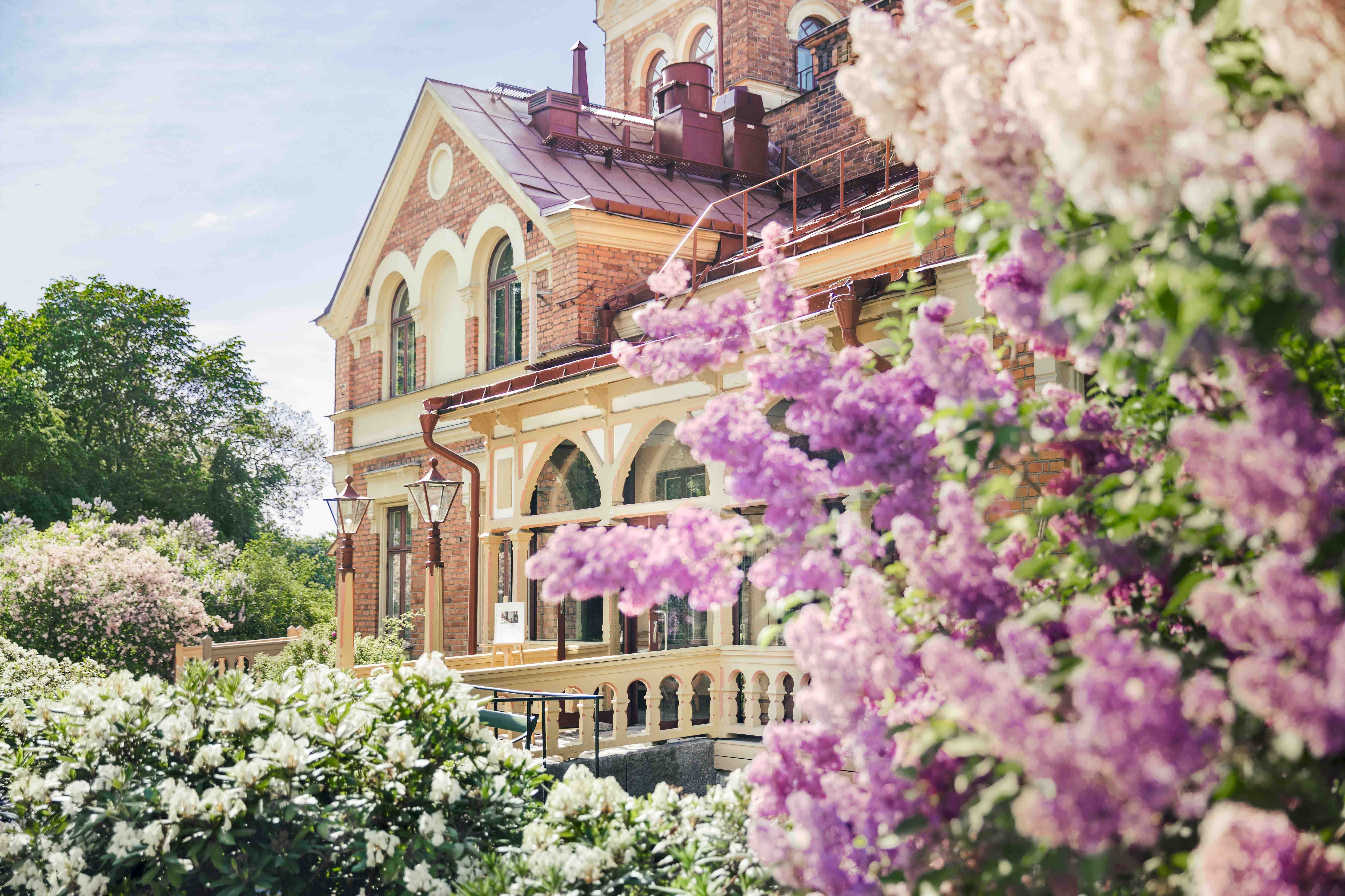 Historic villa at Hotel J framed by blooming lilac bushes and lush spring greenery.