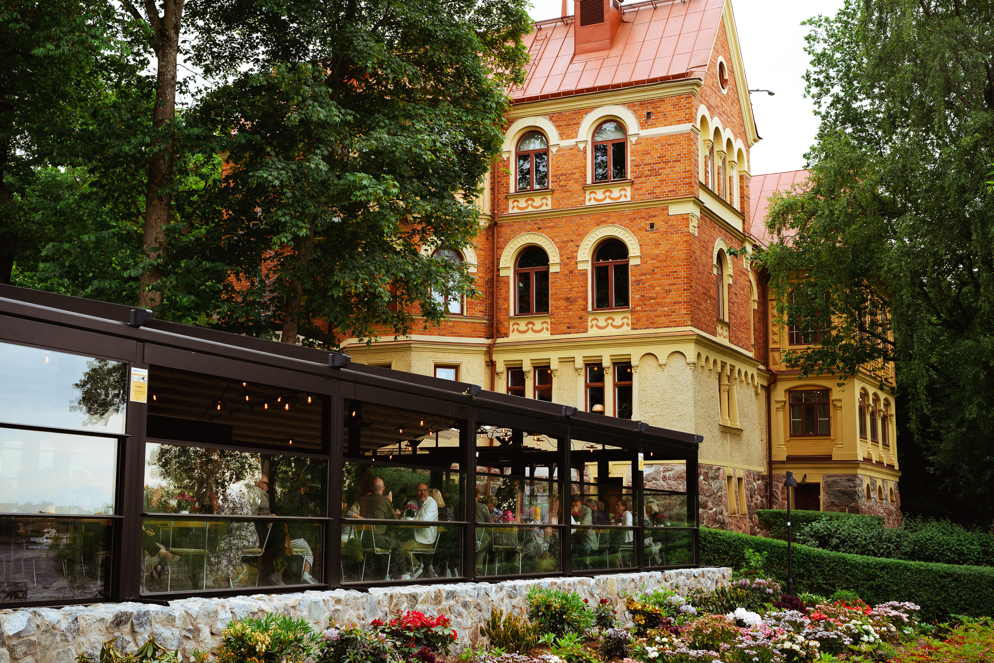 Exterior view of the historic villa at Hotel J with a glass-walled restaurant pavilion and blooming garden in the foreground.