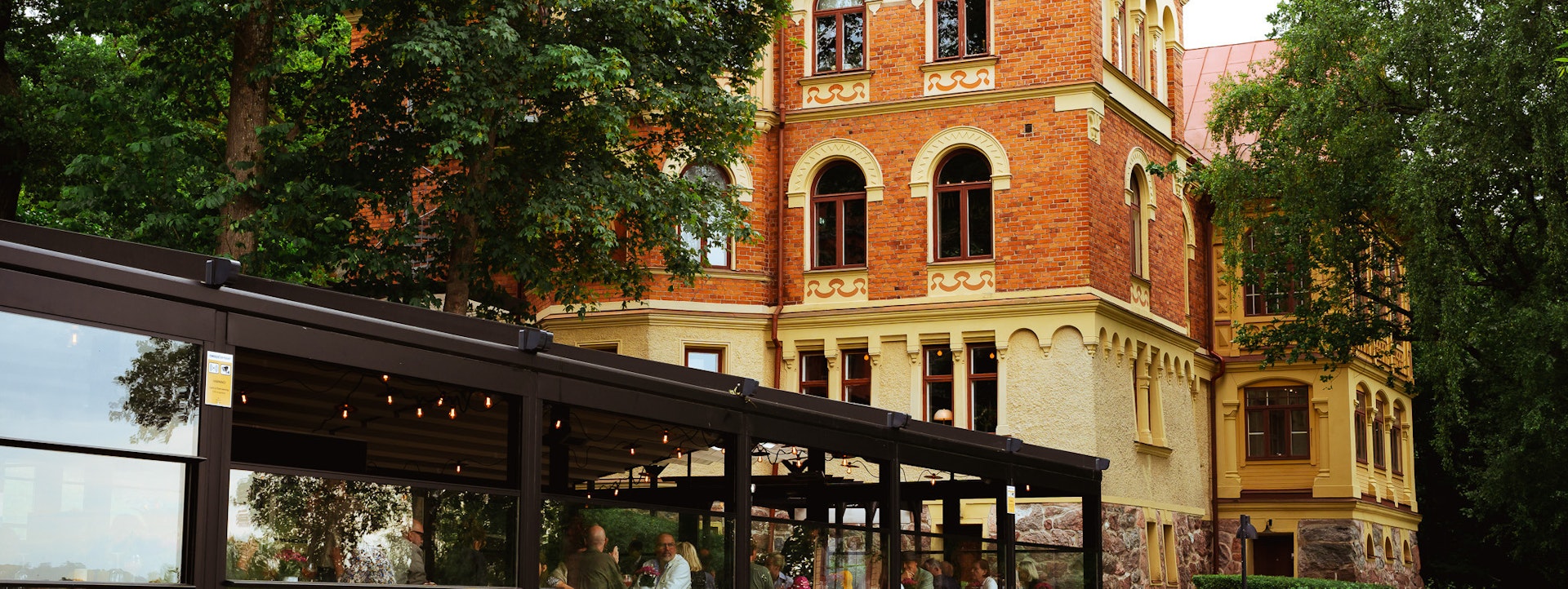 Exterior view of the historic villa at Hotel J with a glass-walled restaurant pavilion and blooming garden in the foreground.