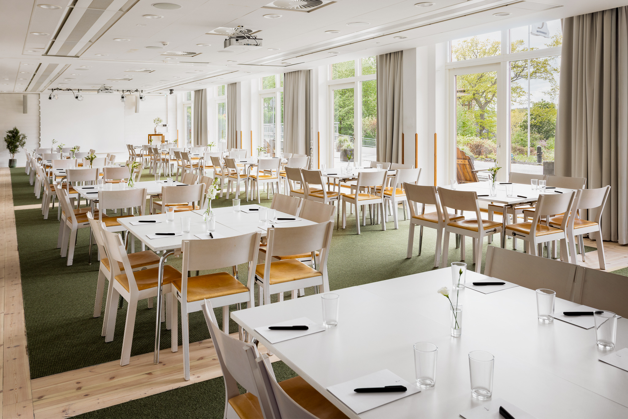 Spacious conference and dining room at Hotel J with white tables, wooden chairs, large windows, and natural light.