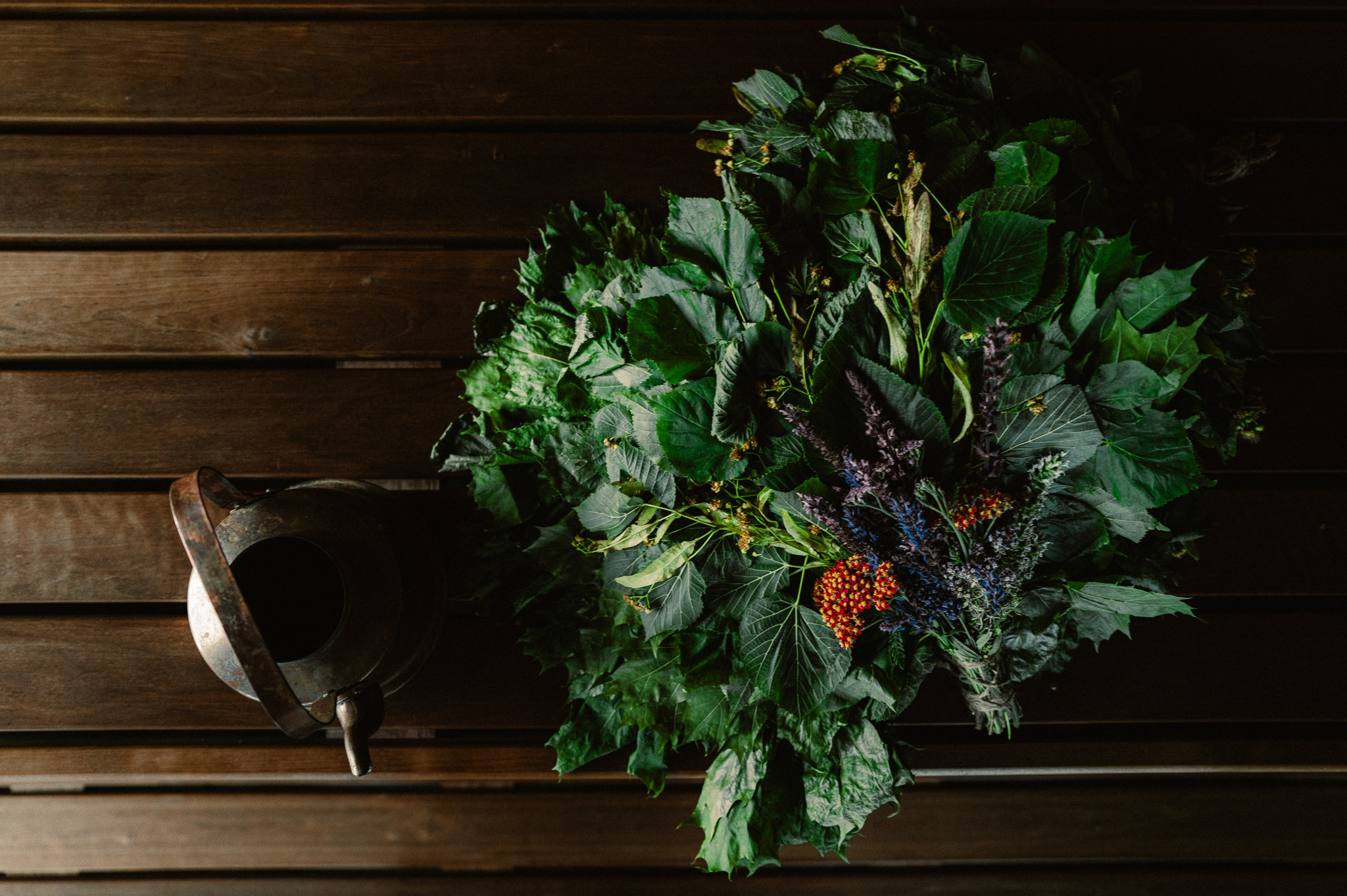 Bouquet d'herbes pour sauna posé sur une surface en bois à côté d'un pot en métal rustique à l'hôtel J.